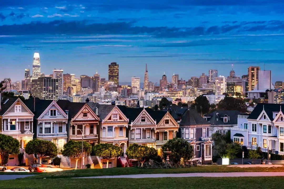 Die berühmten Painted Ladies vom Alamo Square sind in der Dämmerung vor der Skyline von San Francisco zu sehen.